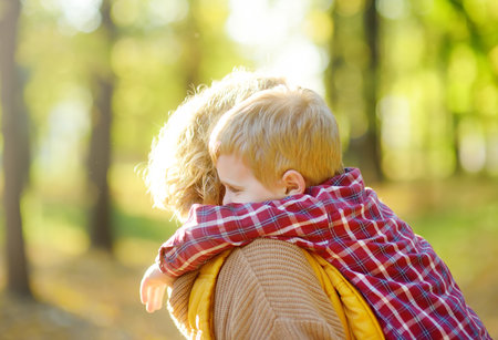 Close-up portrait of a mother and son during a walk in the autumn park. Woman holds her toddler son in her arms and hugs him tenderly. A little boy is having fun and fooling around with his mom.の写真素材