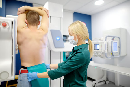 Female radiologist is going to take an Xray of patient in X-ray room of modern clinic. Doctor prepares patient for fluorography. Medical examination of people is prevention of spread of tuberculosisの写真素材