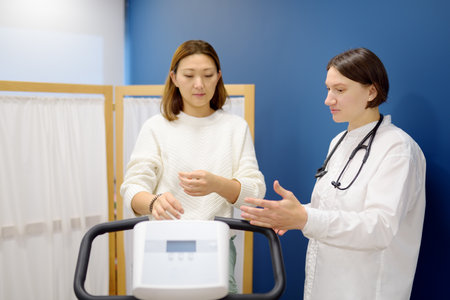 A female cardiologist tests a patient during a bike workout to check the cardiovascular system in...