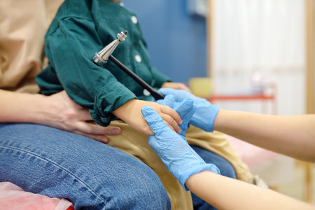 Baby and his mother are being seen by a pediatric neurologist in a modern medical clinic. Doctor conducts tests, checks the reflexes using neurological hammer of a small patient. Highly qualified cureの写真素材