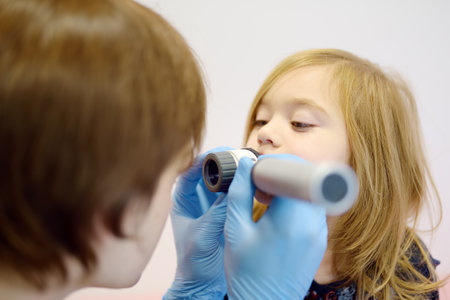 Cute little girl during appointment of dermatologist in modern clinic. Male doctor looking a pimple on a lips of child using dermatoscope. Small baby during an examination by a dermatologistの写真素材