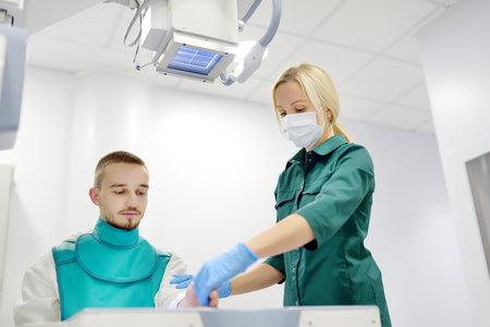Young man having x-ray shot of broken hand in x ray room in modern clinic. Patient wearing in...