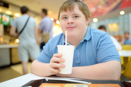 Portrait of a teenager with Down syndrome in a big city. Boy with Down syndrome enjoys food and soda at fast food restaurantの写真素材