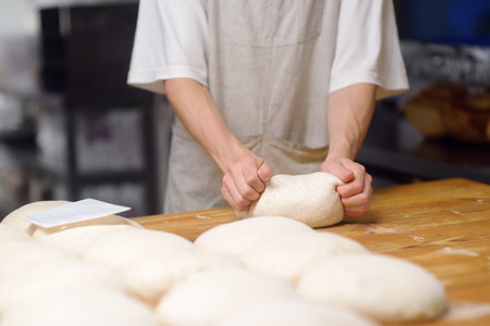 The bakery chef prepares the dough for baking bread. The baker kneads the dough and sets it to fit, baking eco-bread according to an old traditional recipe. Workflow in a local bakery. Ciabatta makingの写真素材