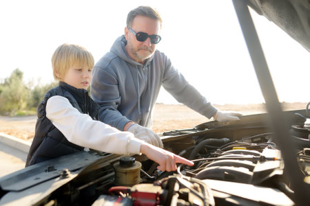 A middle-aged father and a preteen son work on a car during a road trip. DIY car repair and maintenanceの写真素材