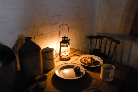 Lamplit Victorian dinner table with lantern, ceramic beer keg and enamel plates and mugsの写真素材
