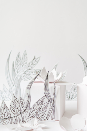 3d paper flowers with painted leaves and stems, white gifts and white paper flowers on the white backgroundの写真素材