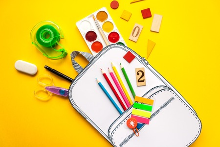 Creative school bag made of paper with school stationery on yellow background. Trendy concept