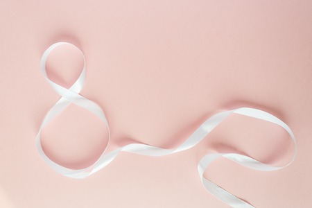 White gift celebration ribbon in 8 digit shape over pale pink backgroundの写真素材
