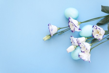 Beautiful white lisianthuses with colorful eggs on light blue background. Spring and Easter holiday concept with copy space.の写真素材