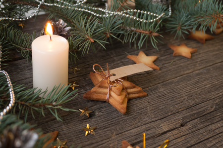 Merry Christmas and Happy New Year. Christmas concept with burning candle, fir tree branches and Christmas cookies in the shape of a stars on old wooden background, selective focus.の写真素材