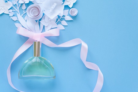 Flower arrangement. Flowers, fragrance, perfume with pink ribbon on blue background. Cut from paper