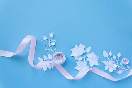 frame with white paper flowers and pink ribbon on blue background. Cut from paper. place your textの写真素材