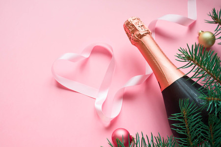 Merry Christmas concept. Bottle champange with fir brunches and christmas balls and pink ribbon in the shape heart on pink background. Present with loveの写真素材