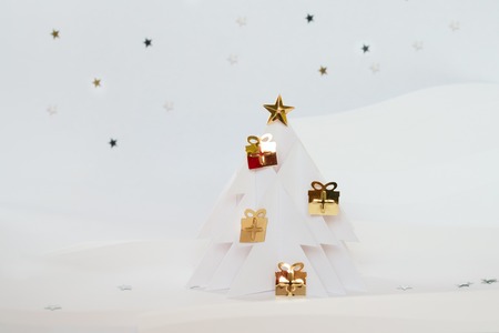 Winter wonderland made of white paper. Christmas tree of white paper decorated with a gold star and gift. Christmas holidays conceptの写真素材