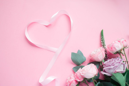Frame of purple and pink roses, white Lisianthus and different flowers and pink ribbon in the shape heart on pink background. Flat lay, top viewの写真素材