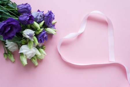 Frame of white Lisianthus and pink ribbon in the shape heart on pink background. Flat lay, top viewの写真素材