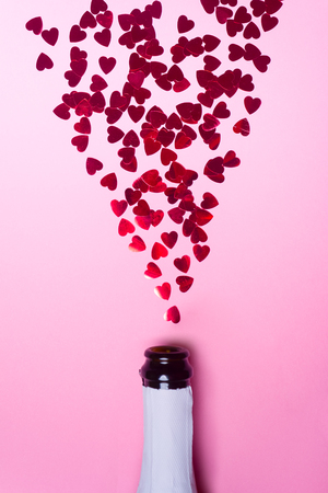 Champagne bottle with heart-shaped sequins on pink background. Valentines day concept. Flat lay.の写真素材