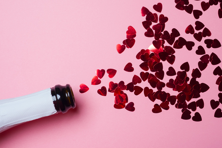 Champagne bottle with heart-shaped sequins on pink background. Valentines day concept. Flat lay.の写真素材