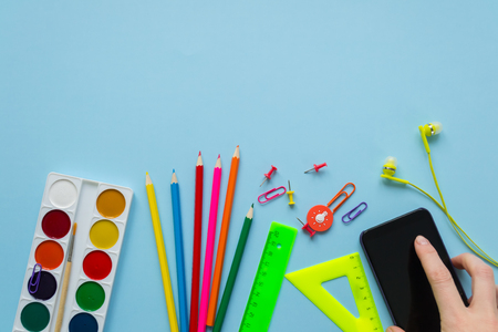 Various stationery and phone on blue background. Holding his phone in his hands. Back to school...