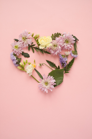 Heart made of different flowers on pink background. Flat lay. Love concept.の写真素材