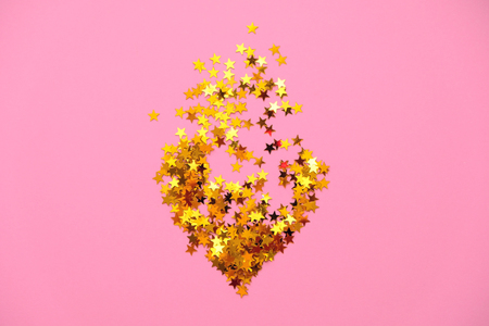 Gold sequins in the shape of a heart on a pink backgroundの写真素材