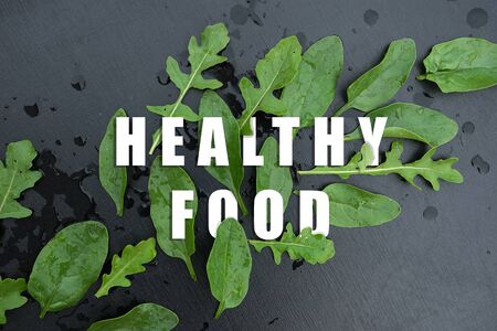 Lettering Haelthy food with spinach and arugula leaves on a black wooden background