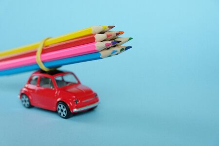 a small red car carries colored pencils. The concept of autumn, back to school