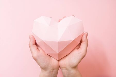 Hands holding a paper polygonal pink heart on pink backgroundの写真素材