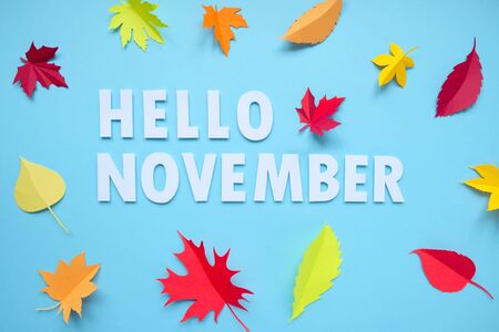 Lettering hello november with autumn leaves red, orange, yellow. Blue background. Letters are cut out of paperの写真素材