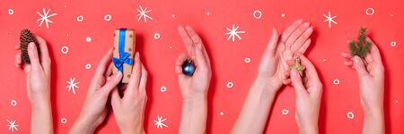 Different female hands holding Christmas elements on red background. Long format for webの写真素材
