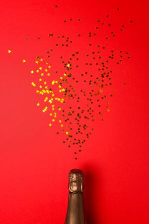 salute from sequins in the form of stars flies out of a bottle of champagne on red background. Congratulation concept.の写真素材