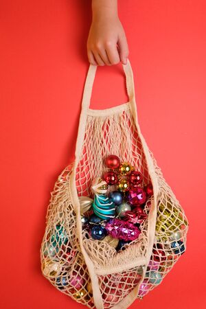 Children's hand holding a string bag with Christmas toys on red background