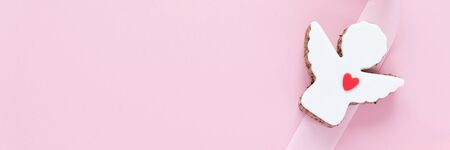 Cookies in the shape of an angel with a pink ribbon on a pink background.の写真素材