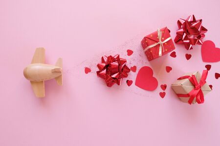 A small wooden toy airplane carries Valentine's elements. Vapor trail of sequins in the shape of heart, gifts, bow and red glitter. Valentine's dayの写真素材