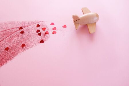 A small wooden toy airplane carries Valentine's elements. Vapor trail of sequins in the shape of heart and red glitter. Valentine's dayの写真素材
