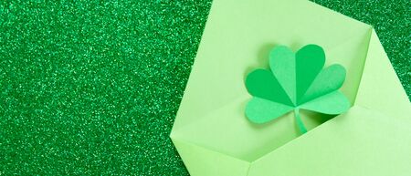 St. Patrick's day, pattern of clovers cut out of paper on a green shiny background