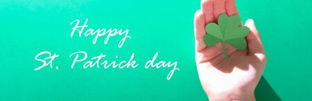 St. Patrick's day, children's hands hold a clover on a green background with the symbols of St....