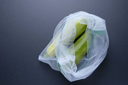 Composition with zucchini in a string bag on a black background. Eco concept, healthy food, vitamins. Zero waste concept.の写真素材