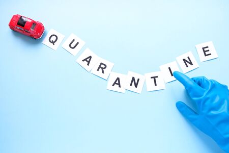 A small red car carries a sign about quarantine. Mass notification. The gloved hand shakes a finger. Concept of quarantine and isolationの写真素材