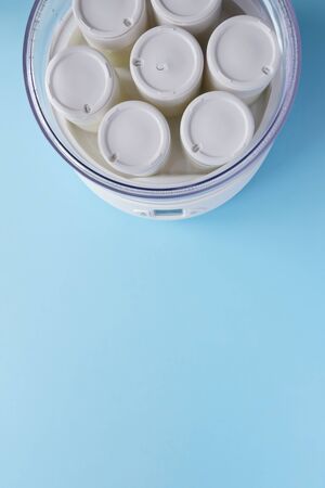 Fermented yogurt in yogurt machine. Homemade greek yogurt in glass jars on light blue background.の写真素材
