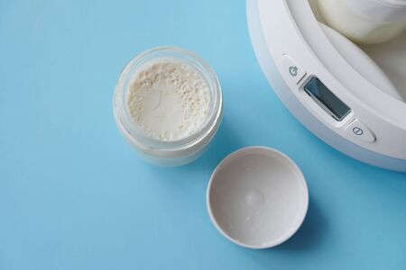 Fermented yogurt in yogurt machine. Homemade greek yogurt in glass jars on light blue background.の写真素材