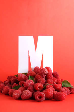 Letter M with fresh raspberries with mint leaves on a red background. Long format for webの写真素材