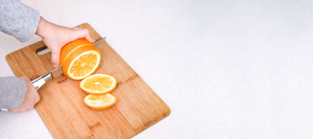 Boys hands cutting fresh orange on kitchenの写真素材
