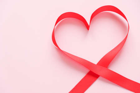 red ribbon in the shape of a heart on a pink backgroundの写真素材