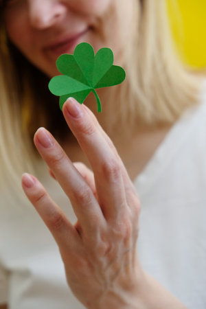 Shamrock in hand of young women in front of her face. Girls face on yellow background. Selective focus.の写真素材