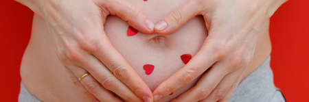 Pregnant Woman holding her hands in a heart shape on her baby bump. Pregnant Belly with fingers...