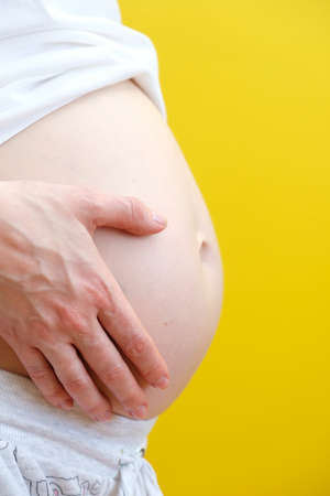 A pregnant woman holding your belly. Close up of a cute pregnant belly. Positive yellow background