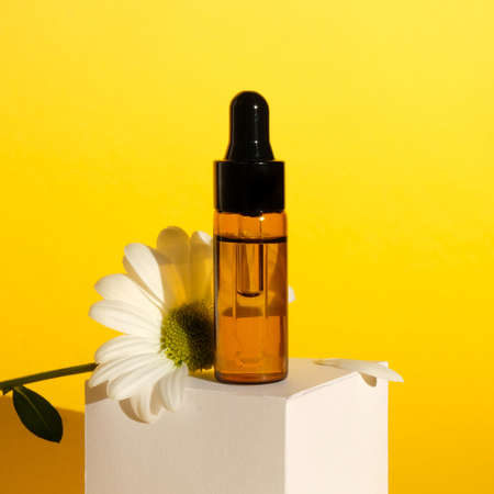 Aromatherapy composition on yellow background. Chamomile essential oil in a glass bottle with...