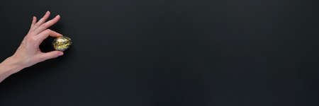 Woman hand holding black easter eggs with gold pattern on black background. Luxury easterの写真素材